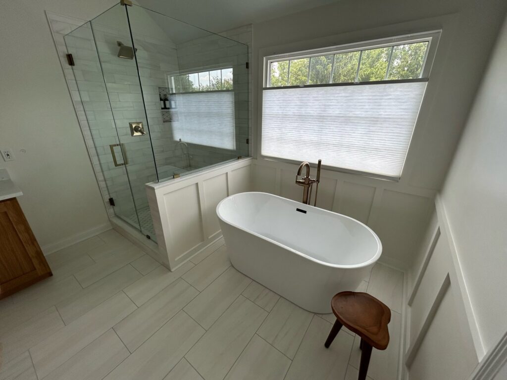 A spacious bathroom remodel with a glass-enclosed shower and a freestanding tub by Benjamin Design - Build in Fishers, IN.