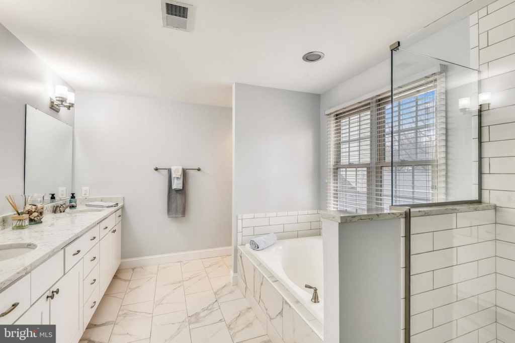 A spacious bathroom renovation with white tiles, a double vanity, bathtub, and walk-in shower by Prestige Services in Annapolis, MD.