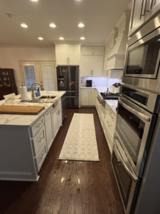A spacious kitchen remodel showcasing white cabinetry, a large island, and dark wood flooring by Cannon & Associates in Montgomery, AL.