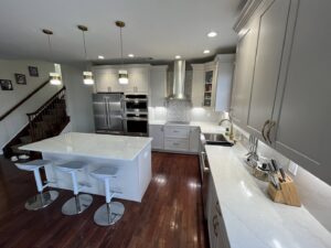 A spacious kitchen remodel featuring light grey cabinets, a large white island, and stainless steel appliances by MPH Design in Philadelphia, PA.