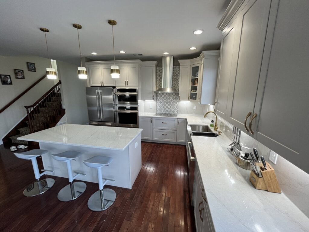 A spacious kitchen remodel featuring light grey cabinets, a large white island, and stainless steel appliances by MPH Design in Philadelphia, PA.