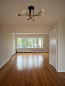 A spacious room with newly installed hardwood flooring and a modern chandelier by Shore Flooring Solutions in Edison, NJ.