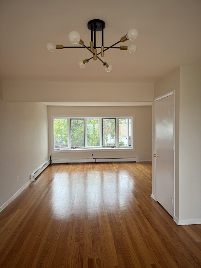 A spacious room with newly installed hardwood flooring and a modern chandelier by Shore Flooring Solutions in Edison, NJ.