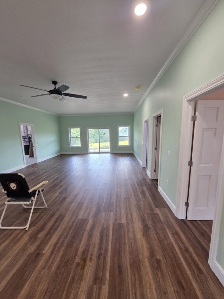 A spacious, newly renovated room with light green walls, wood-look flooring, and a ceiling fan by Ben Nye The Fix-It Guy in Erie, PA.