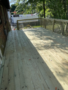 A spacious newly built wooden deck with railings next to a brick house by AC Fence and Ironworks in Philadelphia, PA.