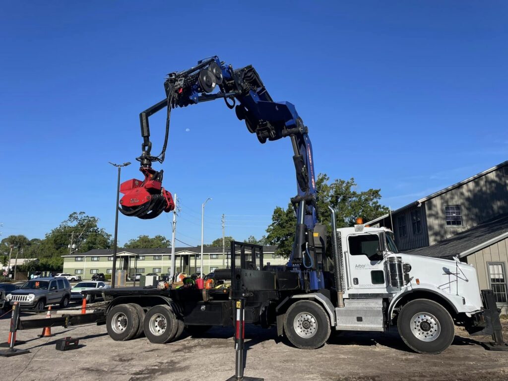 A specialized grapple truck with its arm extended, used for tree debris removal by Royal Oak Tree Services in Jacksonville, FL.