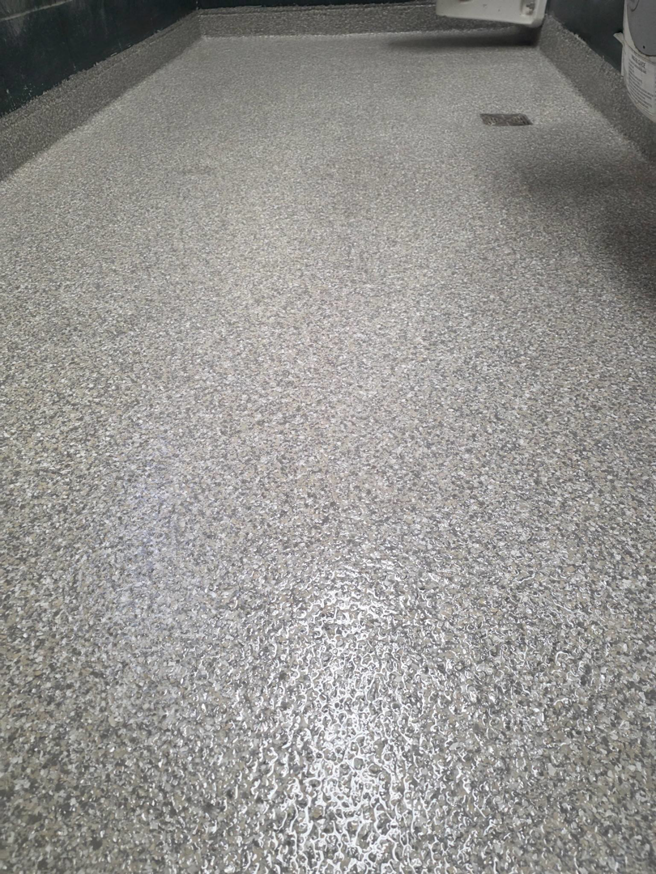 A durable grey speckled epoxy floor installed in a shower area by New Age Decorative Concrete in Broussard, LA.