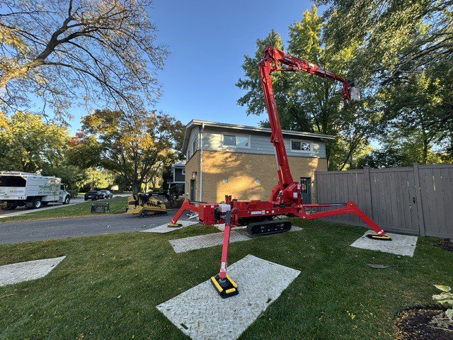 A red spider lift deployed on protective mats in a residential yard by Wildwood Tree Service in Elgin, IL.