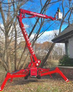 A worker in a red spider lift performing tree trimming services for J's Tree Trimming and Removal, Inc. in Ann Arbor, MI.