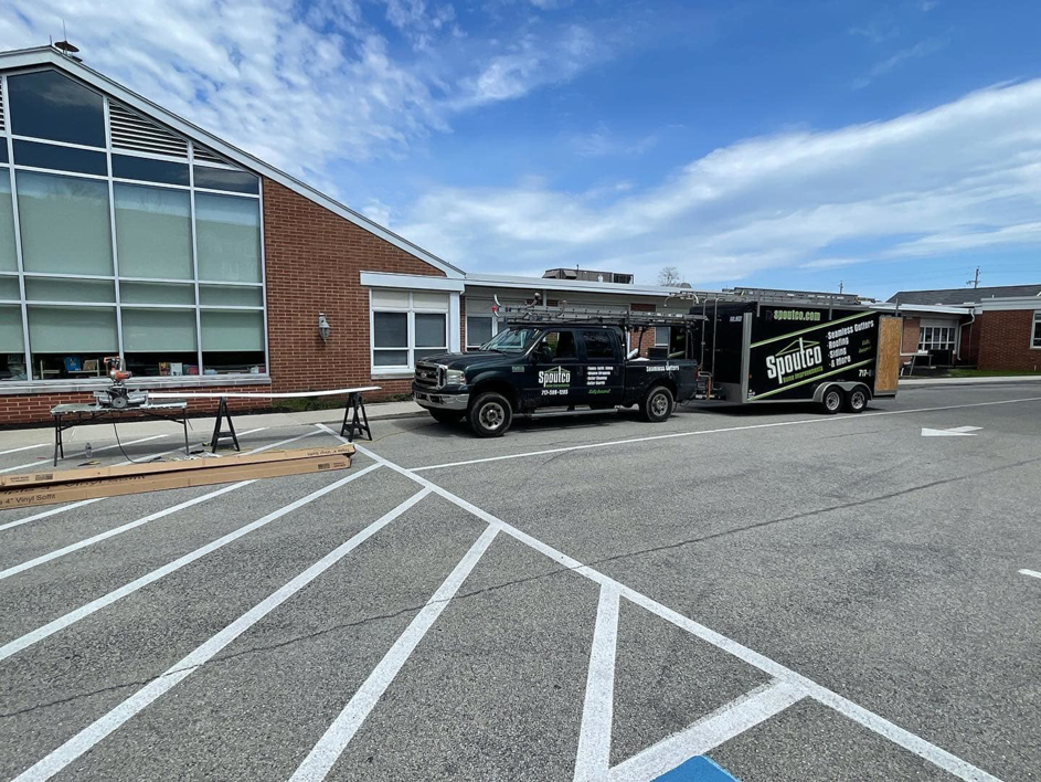 A Spoutco Home Improvements truck and trailer with materials at a commercial building job site in York, PA.