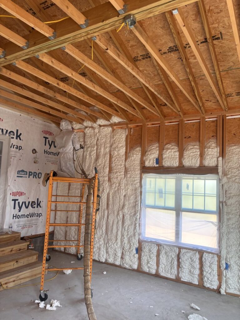A worker on scaffolding applying spray foam insulation to a wall for Off-Axis Spray Foam and Radon Services in Clarksville, TN.