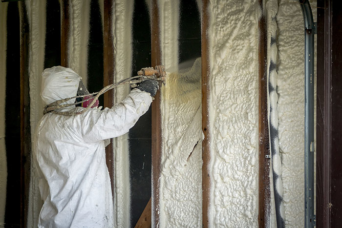 A worker applying spray foam insulation to a wall with exposed studs for Custom Insulation Company, Inc. in Worcester, MA