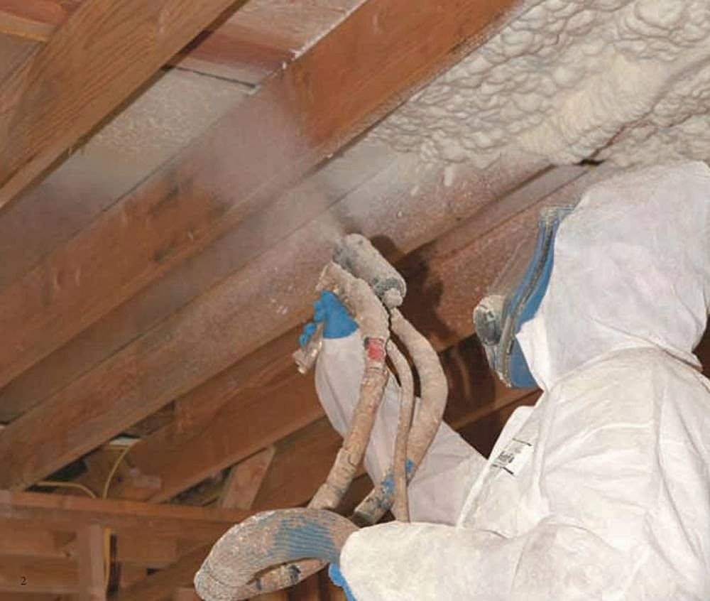 A worker in protective gear applying spray foam insulation to wooden rafters for Spray Foam Solutions Of Erie in Erie, PA.