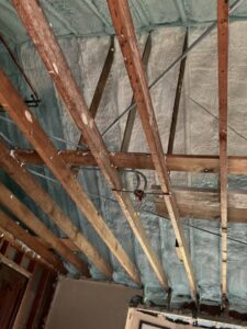 Close-up of spray foam insulation applied to an attic ceiling with exposed wooden beams by Metro Insulation in Rockford, IL.