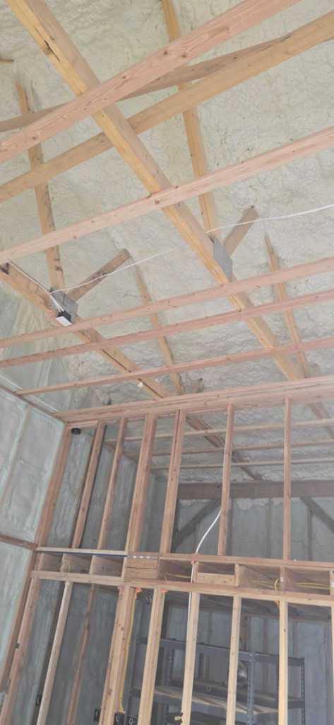 Spray foam insulation covering the ceiling and walls with wooden framing by Tumbarello Insulation in Peyton, CO.