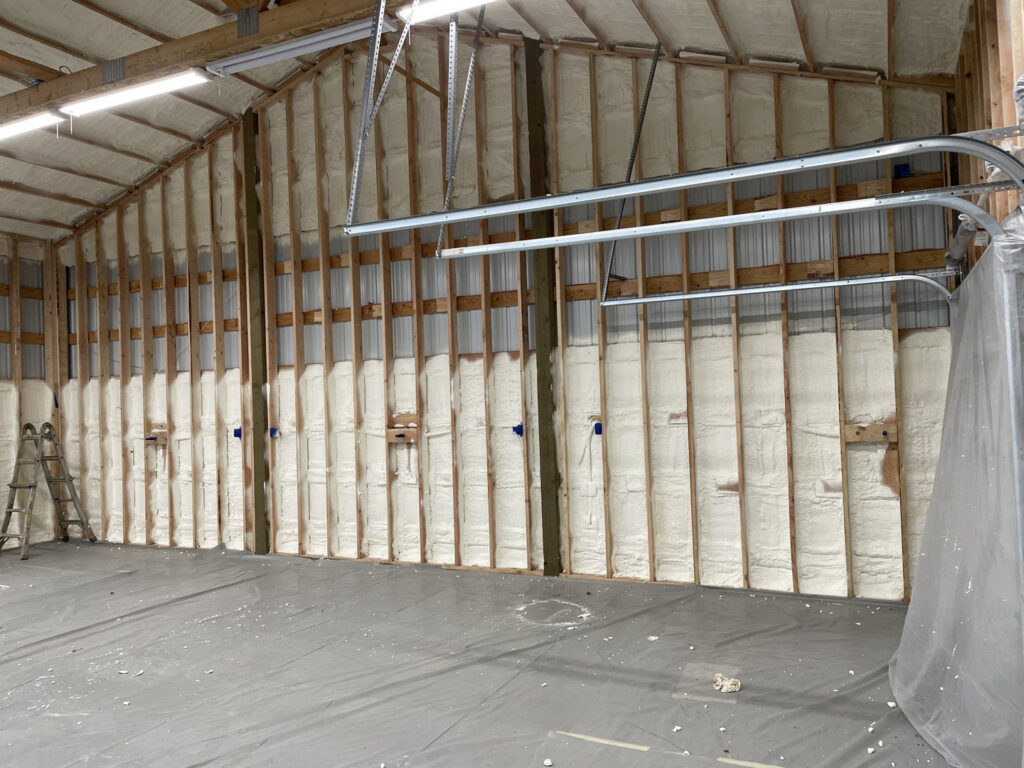 Interior view of a garage or workshop with new spray foam insulation applied between wall studs, installed by Northwest Crawl Space Services in Kent, WA.