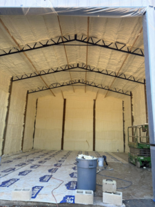 A large room showing spray foam insulation applied to walls and ceiling, with equipment on site from Gulf Coast Spray Foam Insulation & Coatings, LLC in Mobile, AL