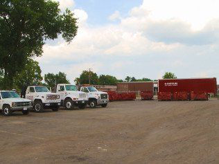 The SS ROLL OFF Dumpsters fleet of trucks and dumpsters parked in a lot in Rockford, IL.