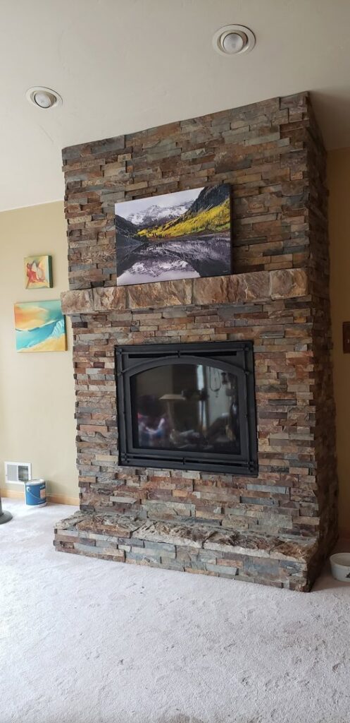 A beautifully installed stacked stone fireplace with a wooden mantel and artwork by The Foundation Guys in Lakewood, CO