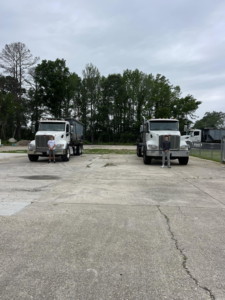 Two staff members standing in front of roll-off trucks, one with a dumpster, at A-1 Roll-Off Rentals, LLC in Baton Rouge, LA.