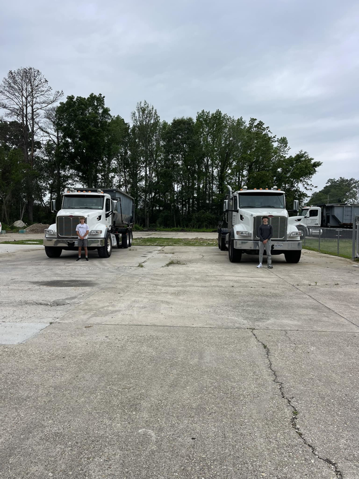 Two staff members standing in front of roll-off trucks, one with a dumpster, at A-1 Roll-Off Rentals, LLC in Baton Rouge, LA.