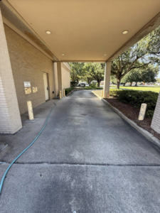 A heavily stained concrete drive-through area with a hose, indicating a pressure washing job by Ducky's Pro Wash in Mobile, AL.