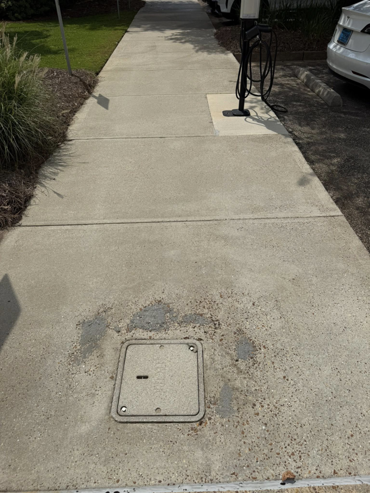 A concrete walkway with dark stains around a utility cover, showing the need for cleaning by Ducky's Pro Wash in Mobile, AL.