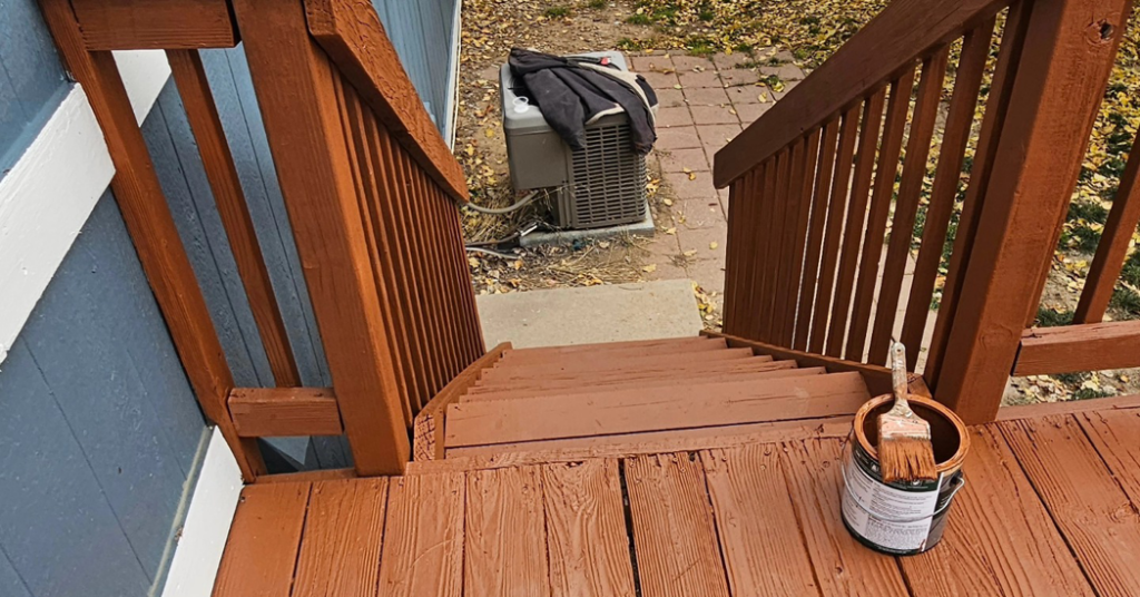 View down newly stained wooden deck stairs with a can of stain and brush, completed by All Hung Up LLC in Littleton, CO.