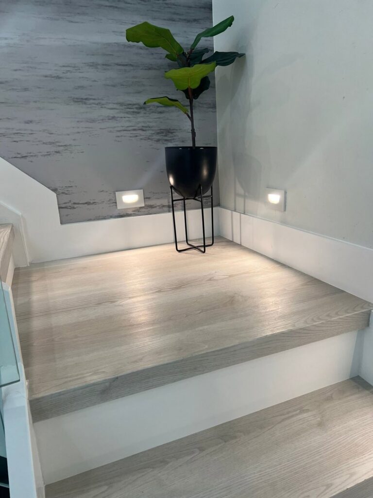 A stair landing showcasing light wood-look flooring, white baseboards, and modern wall sconces, installed by SD Masters in Miami, FL.