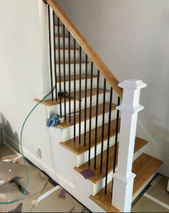 A renovated staircase featuring new wooden treads, white risers, and black metal balusters, indicating a handyman project by Home pro handyman llc in Olathe, KS