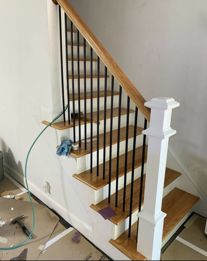A renovated staircase featuring new wooden treads, white risers, and black metal balusters, indicating a handyman project by Home pro handyman llc in Olathe, KS