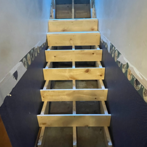 A wooden staircase under construction, showing new treads installed by Chris Pierce Construction in Sioux City, IA.
