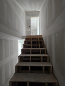 Wooden staircase under construction with new drywall installation by J M Construction & Remodeling in Humble, TX.