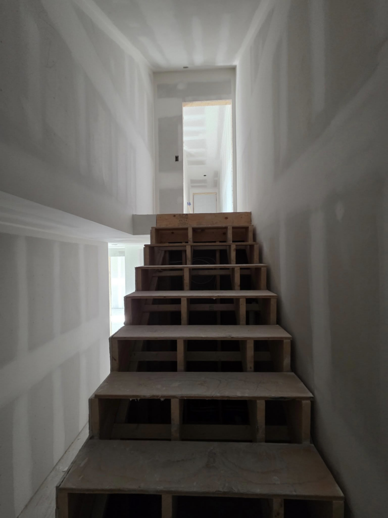 Wooden staircase under construction with new drywall installation by J M Construction & Remodeling in Humble, TX.