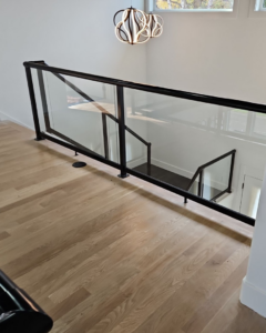 An interior staircase landing showcasing a sleek black framed glass railing system installed by Alpha Railing Company in Tacoma, WA.
