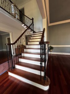 A newly installed staircase with dark wood treads, white risers, and black metal balusters by Albis Morales Painting LLC in Raleigh, NC.