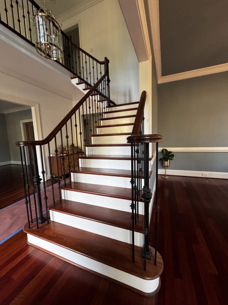 A newly installed staircase with dark wood treads, white risers, and black metal balusters by Albis Morales Painting LLC in Raleigh, NC.