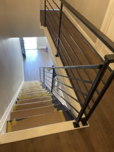 An interior staircase with new black iron railings and protected steps during renovation by AC Fence and Ironworks in Philadelphia, PA.
