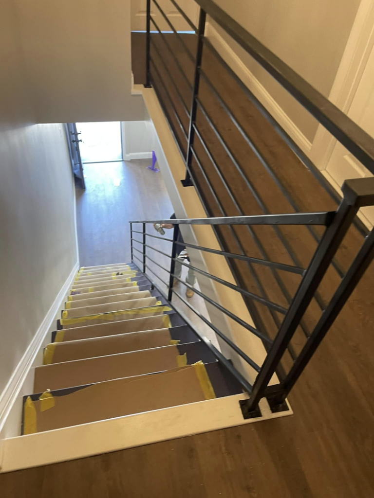 An interior staircase with new black iron railings and protected steps during renovation by AC Fence and Ironworks in Philadelphia, PA.