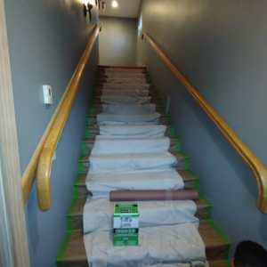 A staircase with grey painted walls and protected steps, showing a painting job in progress by SID Painting in West Hartford, CT.