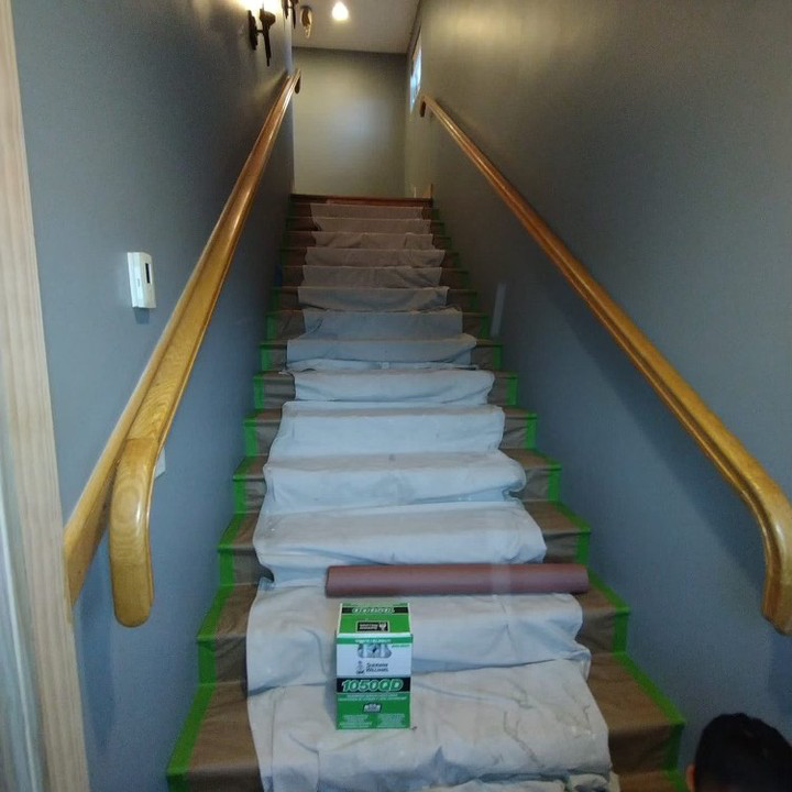 A staircase with grey painted walls and protected steps, showing a painting job in progress by SID Painting in West Hartford, CT.