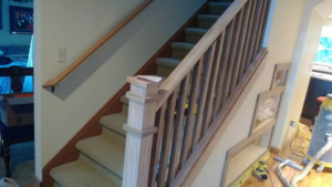 Handyman installing a new wooden staircase railing and newel post at a home by RPG Construction in Virginia Beach, VA.