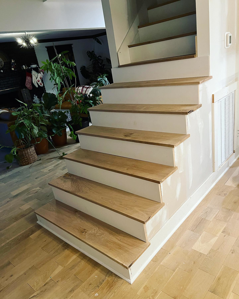A staircase renovation in progress with new wooden treads and white risers by ADAMS Pro Finish in Spring Hill, TN.