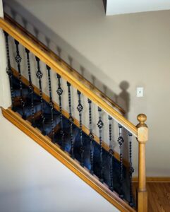 A renovated staircase featuring a wooden handrail and decorative wrought iron balusters by Imagine It Home Improvements Co. in Bethlehem, PA.