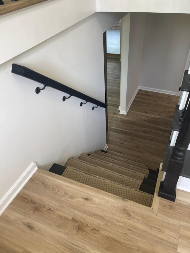 An interior staircase with a black wall-mounted handrail and step protection by AC Fence and Ironworks in Philadelphia, PA.