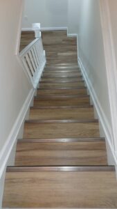 A newly installed staircase with wood-look treads and crisp white railings by Impressive Basements in Westland, MI.