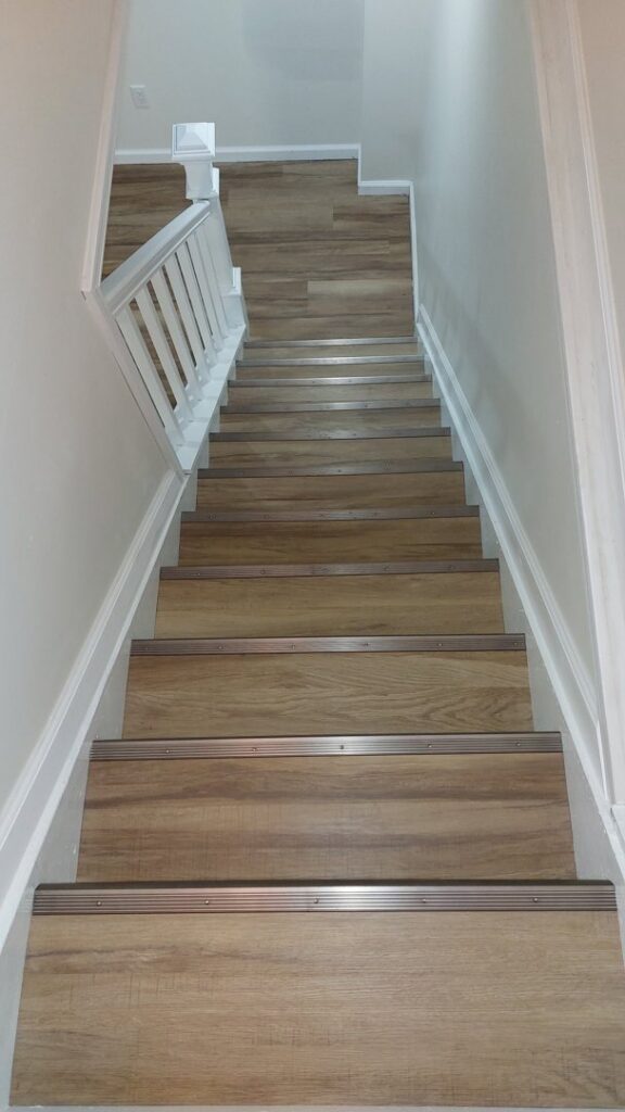 A newly installed staircase with wood-look treads and crisp white railings by Impressive Basements in Westland, MI.
