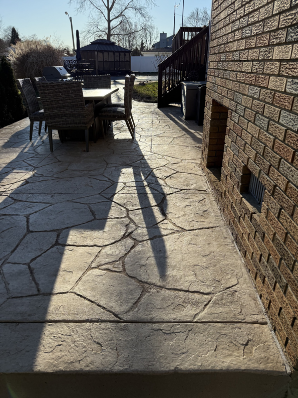 A beautifully installed stamped concrete patio with outdoor seating next to a brick home by Delco Contracting in Toms River, NJ.