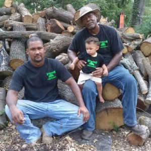 The Stoker Tree Service team in Dallas, TX, including a child, sitting on a large pile of freshly cut logs.