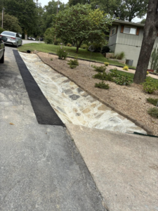 A newly installed stone drainage ditch and landscaping next to a driveway by Wild Hogs Handyman Service in Bentonville, AR.